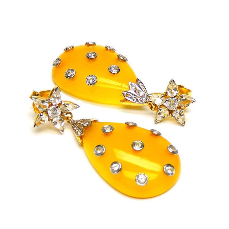 May include: A pair of yellow teardrop-shaped earrings with a star-shaped diamond cluster at the top and smaller diamonds scattered across the teardrop.