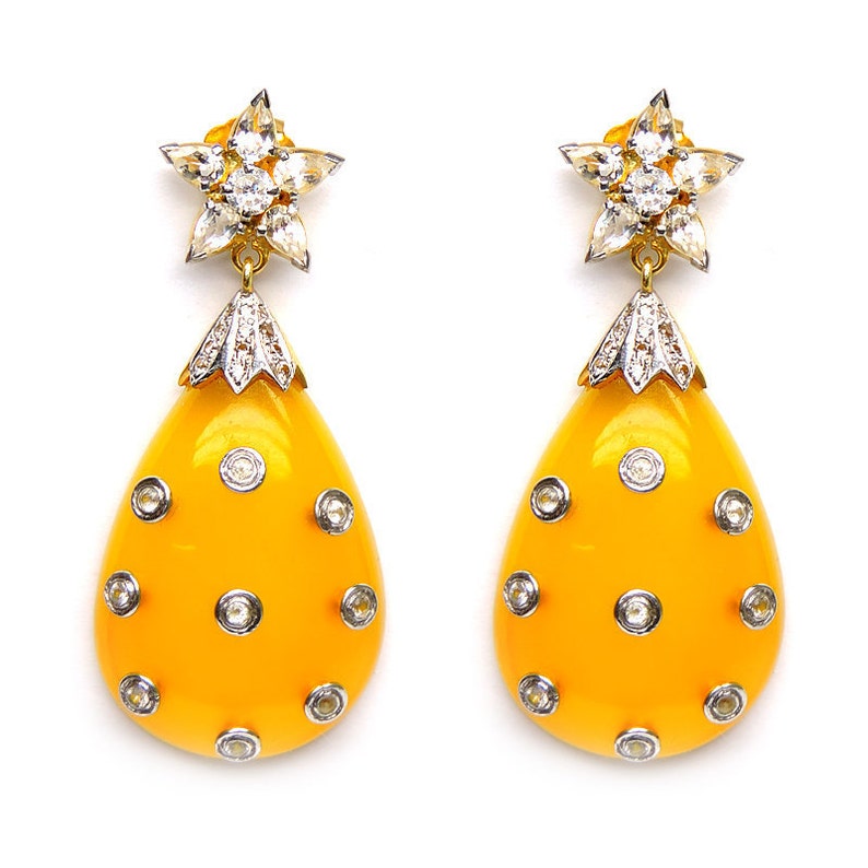 May include: A pair of yellow teardrop-shaped earrings with a star-shaped diamond cluster at the top and smaller diamonds set around the teardrop.