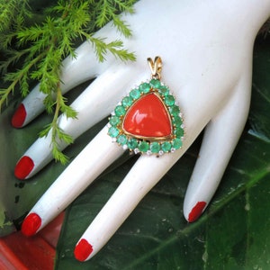 May include: A triangular pendant featuring a large, bright red coral gemstone surrounded by a halo of smaller green emeralds and white diamonds.