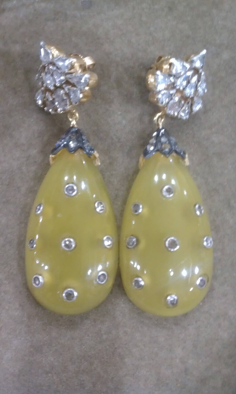 May include: A pair of yellow teardrop-shaped earrings with silver and black accents. The earrings are adorned with small, clear stones.