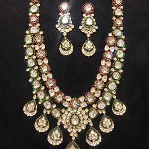 Pu&ograve; includere: Una collana in oro a due livelli con pietre verdi e rosse e orecchini abbinati. La collana ha un design a forma di lacrima con pi&ugrave; piccole lacrime che pendono dalla parte inferiore.