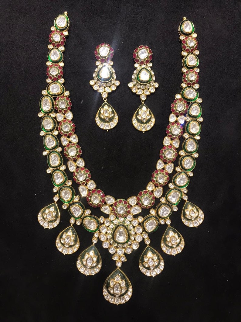 Pu&ograve; includere: Una collana in oro a due livelli con pietre verdi e rosse e orecchini abbinati. La collana ha un design a forma di lacrima con pi&ugrave; piccole lacrime che pendono dalla parte inferiore.