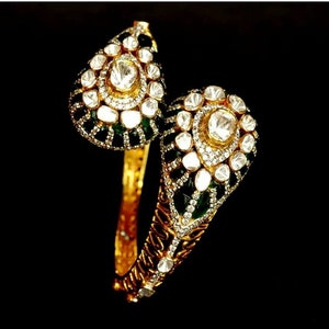 Pu&ograve; includere: Un braccialetto rigido in oro con un designo verde e bianco. Il braccialetto &egrave; decorato con piccoli diamanti ed smeraldi.