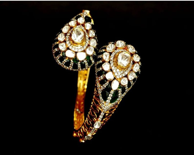 Pu&ograve; includere: Un braccialetto rigido in oro con un designo verde e bianco. Il braccialetto &egrave; decorato con piccoli diamanti ed smeraldi.