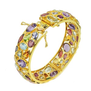 May include: A gold bangle bracelet with a hinged clasp. The bracelet is set with a variety of colorful gemstones, including amethyst, citrine, aquamarine, and ruby.
