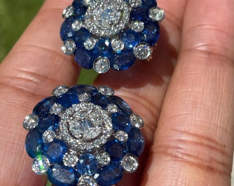 Op de afbeelding: Een paar zilveren oorbellen met een cluster van blauwe saffieren en diamanten in een bloemmotief.