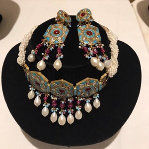 May include: A gold and turquoise necklace and earrings set with pearl accents. The necklace features a geometric design with red stones and the earrings are drop style.