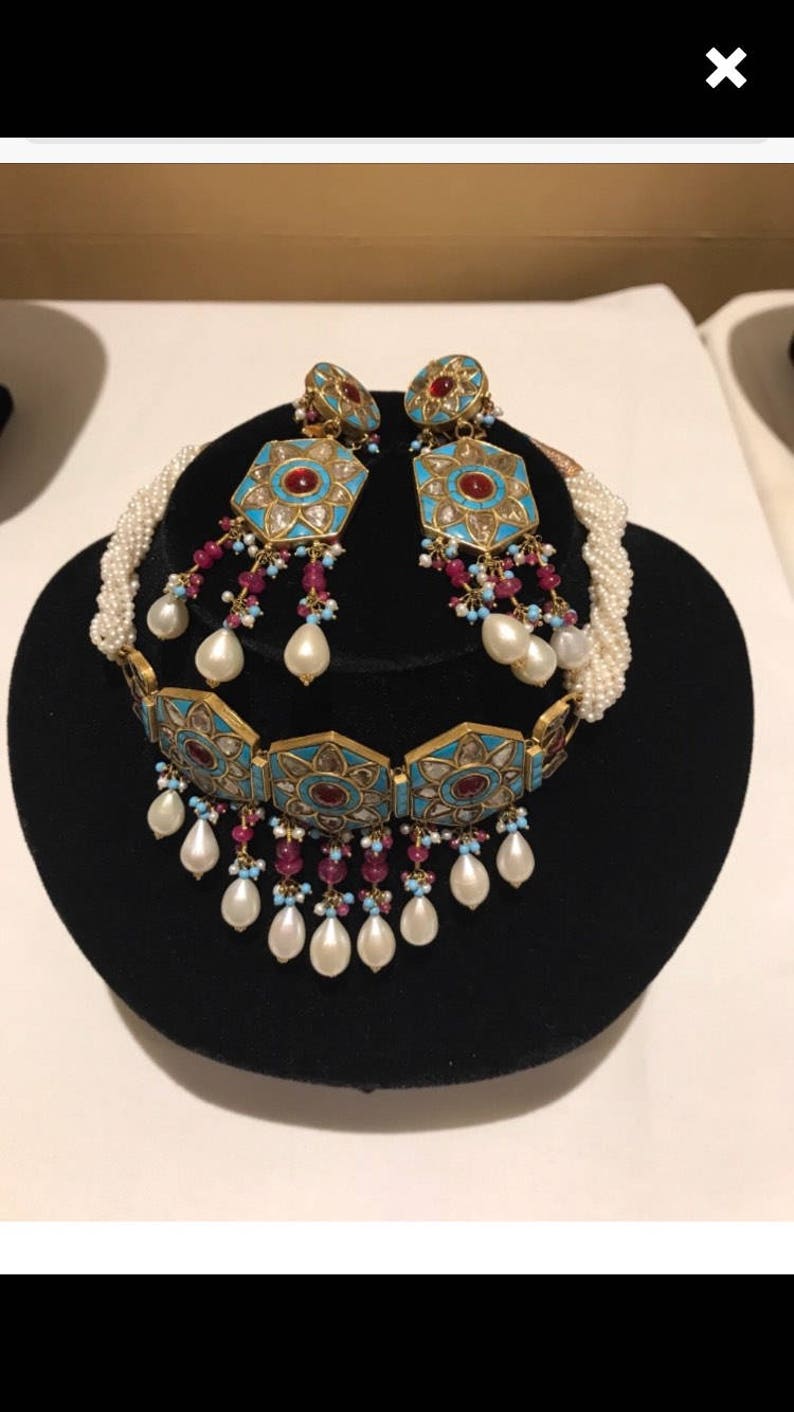 May include: A gold and turquoise necklace and earrings set with pearl accents. The necklace features a geometric design with red stones and the earrings are drop style.