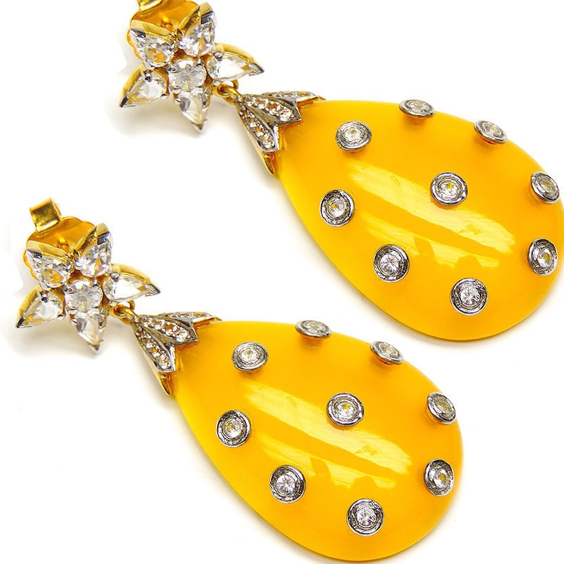 May include: A pair of yellow teardrop-shaped earrings with a cluster of clear rhinestones at the top and smaller clear rhinestones around the edges of the teardrop.
