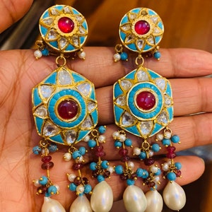 May include: A pair of gold earrings with turquoise and red stones, and pearl drops. The earrings have a hexagonal shape with a central red stone surrounded by smaller stones.