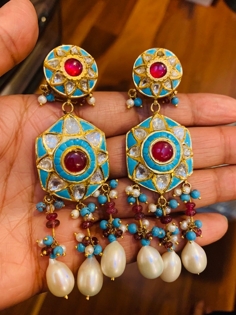 May include: A pair of gold earrings with turquoise and red stones, and pearl drops. The earrings have a hexagonal shape with a central red stone surrounded by smaller stones.