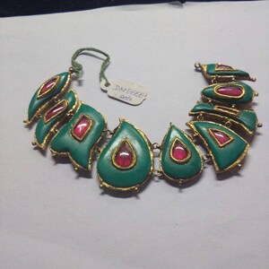 May include: A green and gold necklace with red gemstone accents. The necklace is made of metal and has a teardrop shape. The tag on the necklace reads "DNEECE 5213".