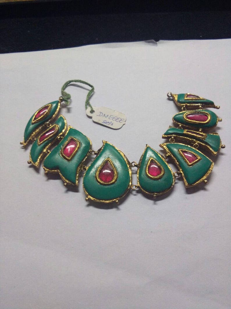May include: A green and gold necklace with red gemstone accents. The necklace is made of metal and has a teardrop shape. The tag on the necklace reads "DNEECE 5213".