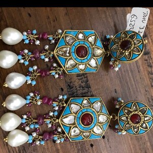 May include: A pair of gold earrings with blue and turquoise enamel, white pearls, and red gemstones. The earrings feature a hexagonal design with a floral motif and the text "EE OWL G22".