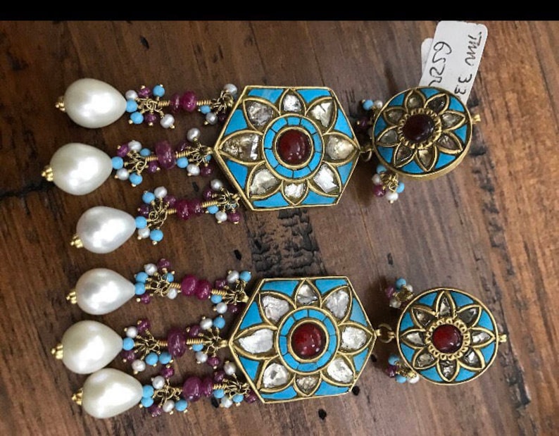 May include: A pair of gold earrings with blue and turquoise enamel, white pearls, and red gemstones. The earrings feature a hexagonal design with a floral motif and the text "EE OWL G22".