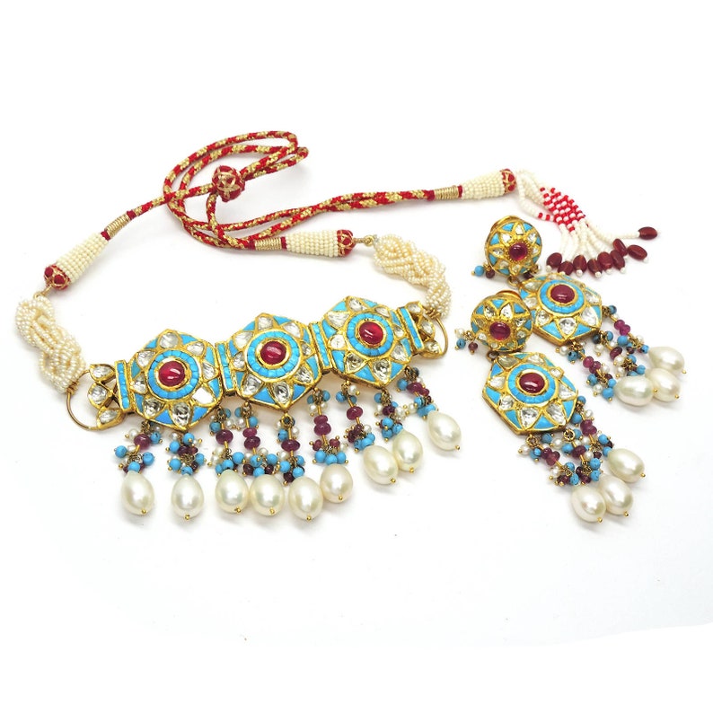 May include: A gold necklace and earrings set with turquoise and red stones. The necklace has a central piece with three large, ornate, turquoise and red stones. The earrings are drop earrings with a large, ornate, turquoise and red stone. The set is decorated with pearls.