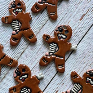 May include: A collection of brown gingerbread-shaped ornaments with a glossy finish. Each figure features a distressed appearance with exposed white rib cages, pink flesh accents, and dark, hollow eye sockets with a single visible eye.