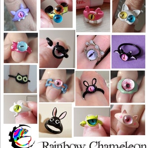 May include: A collection of handmade rings featuring various eye designs. The rings are made with different materials, including metal, plastic, and resin. The eyes are painted in various colors, including blue, green, pink, and yellow. The rings are all unique and eye-catching.