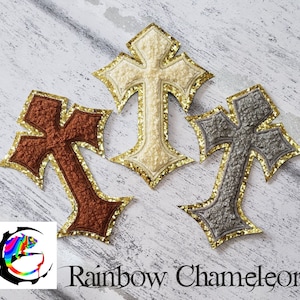 May include: Three felt cross patches with gold glitter trim. The crosses are brown, grey, and white.