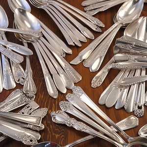 May include: A large collection of vintage silver spoons with ornate designs. The spoons are arranged in a random pattern on a wooden surface.