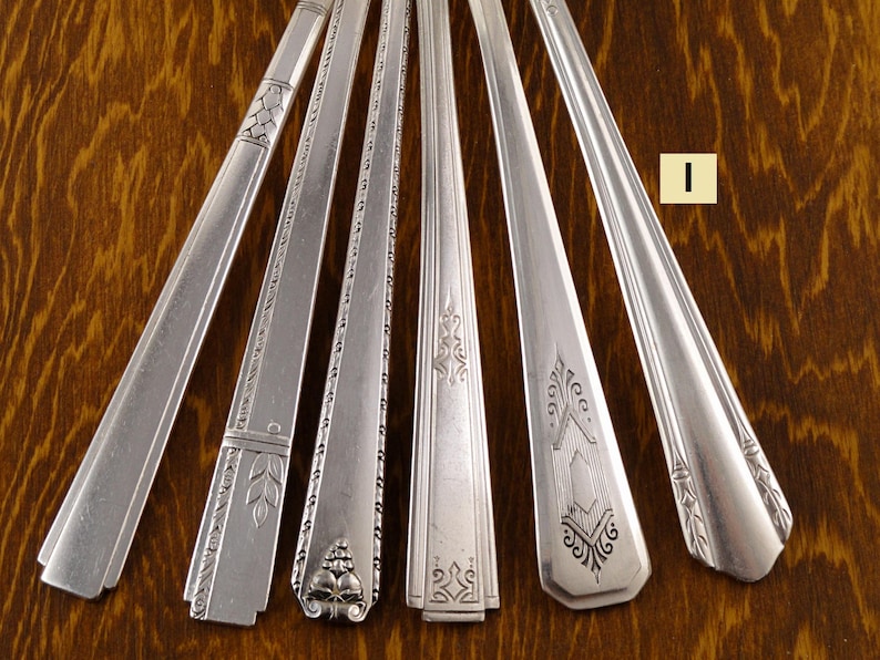 May include: A collection of vintage silver flatware, including spoons and forks, arranged on a wooden surface. Each piece features unique decorative patterns and designs, showcasing the craftsmanship of the era. The silverware is displayed in a fan-like arrangement.