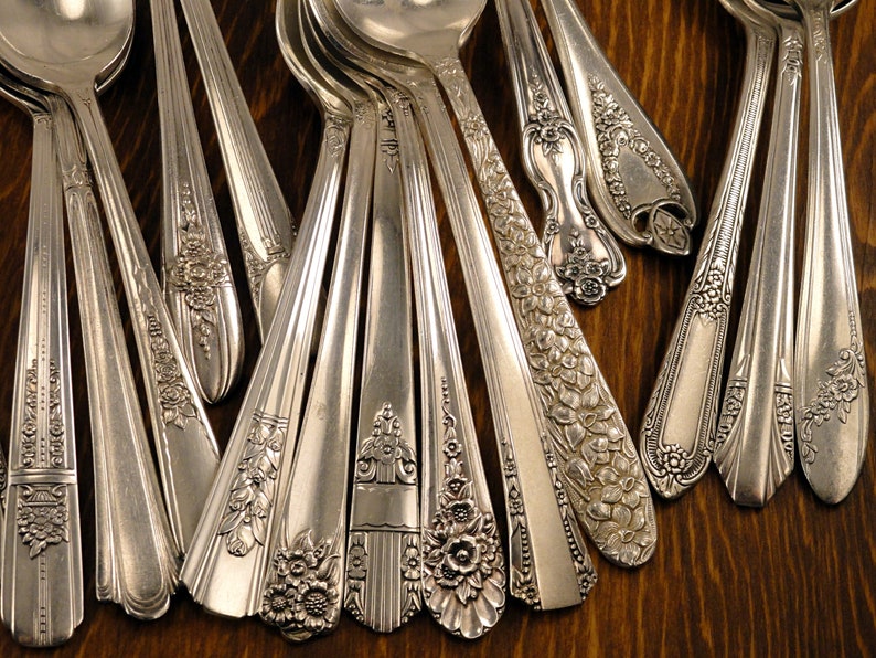 May include: A collection of antique silver spoons and serving utensils with ornate floral and geometric designs. The spoons are arranged on a dark wooden surface, showcasing their intricate patterns and polished finish.