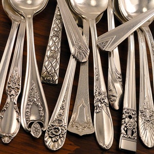 May include: A collection of vintage silver spoons with ornate designs. The spoons have intricate floral patterns and are arranged in a fan shape.