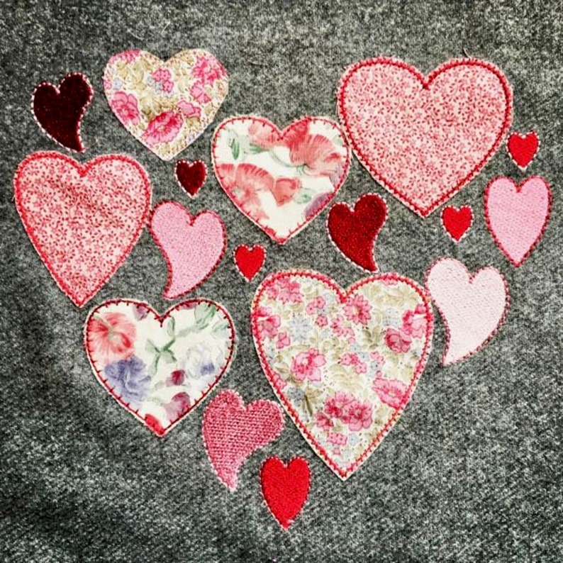 Op de afbeelding: Een grijze stoffen achtergrond met een grote hartvorm gemaakt van kleinere harten. De harten zijn in verschillende tinten roze en rood, sommige met bloemmotieven.