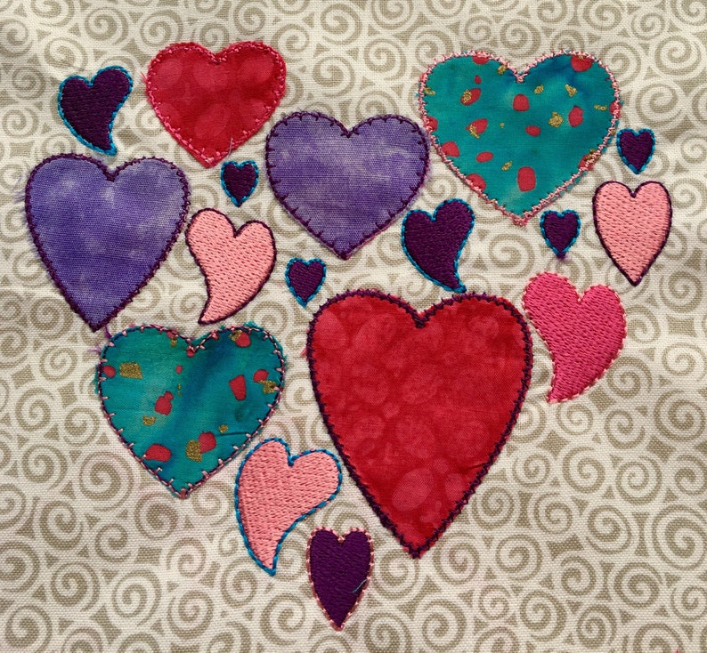 Op de afbeelding: Een verzameling van stoffen harten in verschillende kleuren en patronen, waaronder roze, rood, paars en teal, genaaid op een beige stoffen achtergrond met een wervelend patroon.