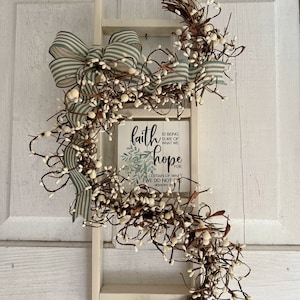 May include: White wooden ladder with a green and white striped ribbon bow and a white berry garland. A small wooden sign with the words "faith is being sure of what we hope for & certain of what we do not see - Hebrews 11:1" is hanging on the ladder.