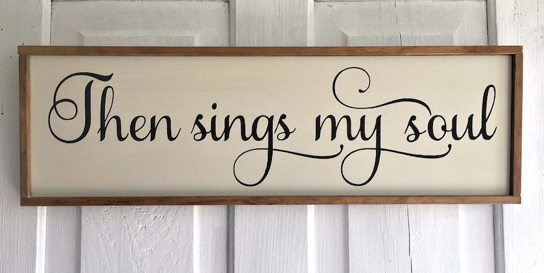 May include: A wooden sign with a cream background and a black cursive inscription that reads "Then sings my soul".