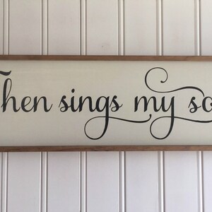 May include: A wooden sign with a white background and a black inscription that reads "Then sings my soul".