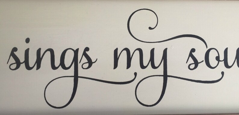 May include: A white wooden sign with black cursive lettering that reads "sings my soul".