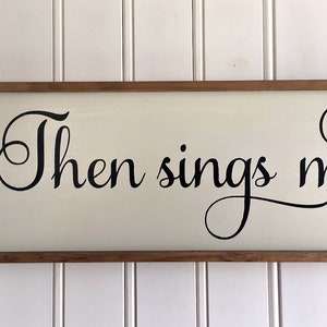 May include: A wooden sign with a white background and black lettering. The sign reads "Then sings my soul".