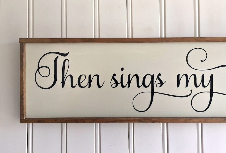 May include: A wooden sign with a white background and black lettering. The sign reads "Then sings my soul".