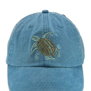May include: A blue denim baseball cap with an embroidered sea turtle design. The turtle is green and brown with a white outline.