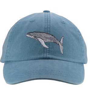 May include: A blue denim baseball cap with an embroidered gray whale design.