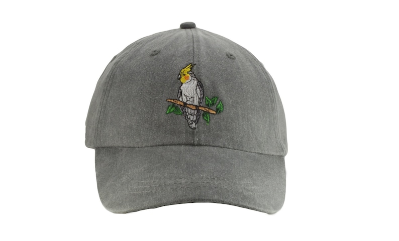 May include: A gray cotton baseball cap with an embroidered image of a yellow-crested cockatiel perched on a branch.