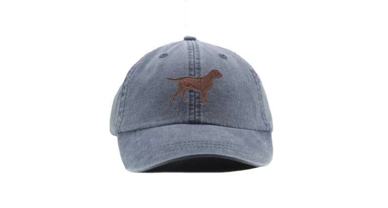 May include: A blue denim baseball cap with a brown embroidered image of a dog.