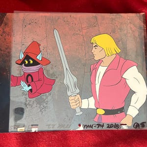 May include: Animation cel featuring two cartoon characters. One character is a muscular blond man in pink and white attire, holding a silver sword. The other is a small, red-robed figure with a purple scarf and a pointed hat. The background is a gray stone wall.