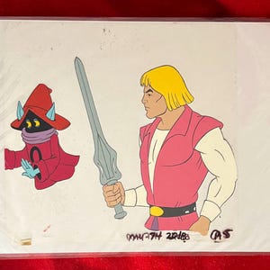 Puede incluir: Celda de animaci&oacute;n con dos personajes de la serie He-Man y los Masters del Universo. Un personaje es He-Man, sosteniendo una espada, y el otro es Orko. La celda est&aacute; en una funda de pl&aacute;stico.