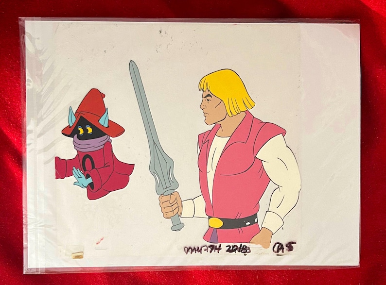Puede incluir: Celda de animaci&oacute;n con dos personajes de la serie He-Man y los Masters del Universo. Un personaje es He-Man, sosteniendo una espada, y el otro es Orko. La celda est&aacute; en una funda de pl&aacute;stico.