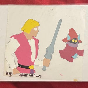 Puede incluir: Celda de animaci&oacute;n con dos personajes de dibujos animados. Un hombre rubio con ropa rosa y blanca sostiene una espada gris. A su lado, un personaje vestido de rojo con bufanda morada y sombrero con cuernos. La imagen tiene texto en la parte inferior.