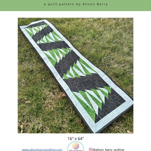 Puede incluir: Un patrón de colcha verde y negro llamado "Cold Snap" de Alison Barry Quilting. La colcha mide 40,6 cm por 162,6 cm y presenta un diseño geométrico de triángulos.