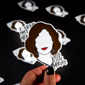 May include: A sticker with a brown-haired woman's face, red lips, and the text "I THINK MOST MEN NEED A LITTLE PRACTICE." The sticker is held by a hand against a black background with similar stickers.