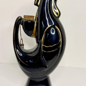 Puede incluir: Una jarra de cerámica negra con forma de gallo y detalles dorados. La botella vintage tiene un tapón de corcho y un asa. Esta pieza decorativa es una adición única a cualquier bar o cocina.