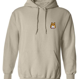 Könnte beinhalten: Beigefarbener Kapuzenpullover mit Kängurutasche und Kordelzug. Auf der linken Brust befindet sich ein kleines, gesticktes Cartoon-Corgi-Gesicht. Der Markenname "JOES USA" ist auf der Kapuze aufgedruckt.