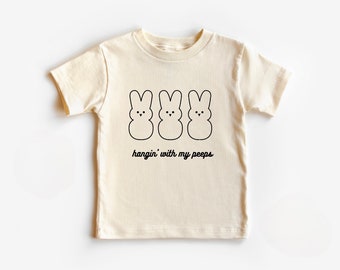 Peut inclure: Un t-shirt à manches courtes de couleur crème avec un motif noir de trois Peeps de dessin animé et le texte "hangin' with my peeps".