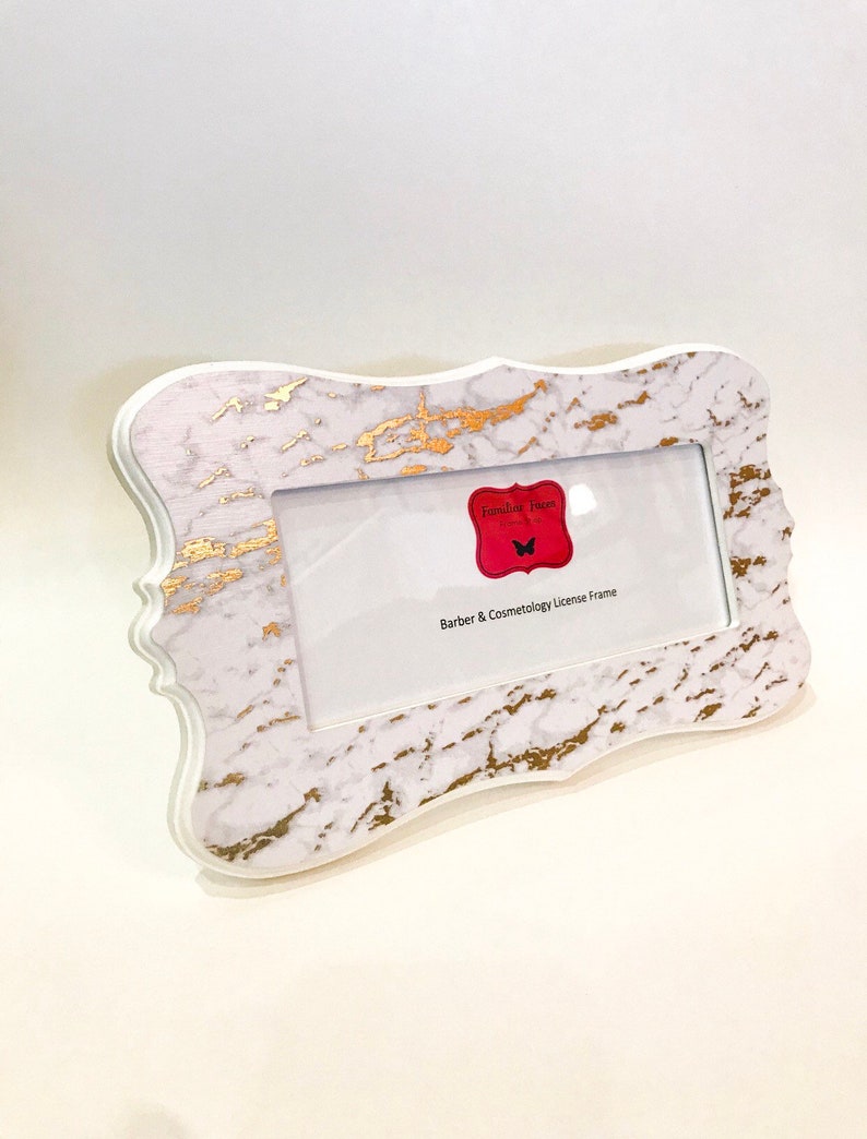 May include: White and gold marble-patterned license frame with a decorative edge. The frame has a rectangular opening for a license and a red label with the text "Familiar Faces" and "Barber & Cosmetology License Frame".