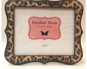Puede incluir: Un marco de fotos decorativo con un estampado de leopardo. El marco tiene un diseño de borde festoneado único y presenta el texto "Familiar Faces Frame Shop" y las dimensiones 20 x 25 cm.